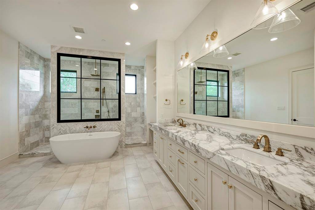 Luxurious spa-inspired primary bathroom showcases a freestanding soaking tub, dual vanities with honed Calacatta Vagli quartzite countertop, a built-in makeup station, and an opulent rain-and-body shower system—all wrapped in elegant porcelain tile.