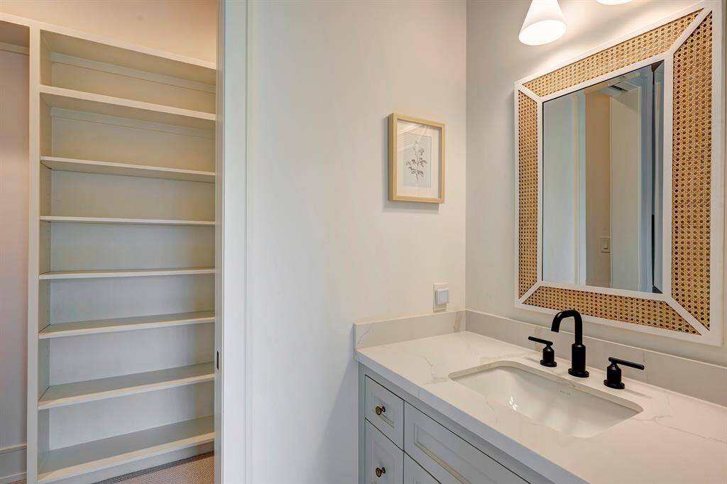 The ensuite bath includes a Statuario quartz countertop, matte black fixtures, a rattan-trimmed designer mirror, and a walk-in shower with a tiled shampoo niche. A spacious walk-in closet with custom built-in shelving completes the suite.
