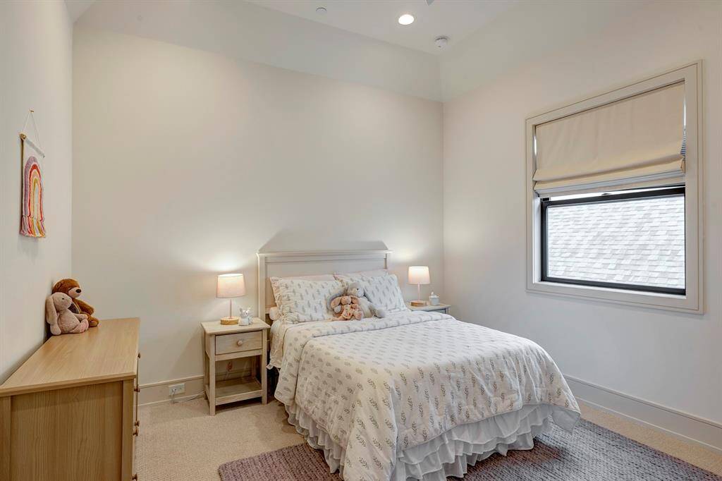 This cozy secondary bedroom features plush carpeting, a cove ceiling, and custom window treatments from The Shade Store for a soft, sophisticated touch.