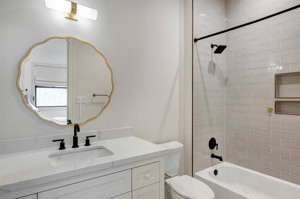 The ensuite bath is beautifully appointed with a tub/shower combo, a sleek shampoo niche, and a Statuario quartz countertop. Matte black fixtures and a designer scalloped mirror elevate the space with modern elegance and personality.