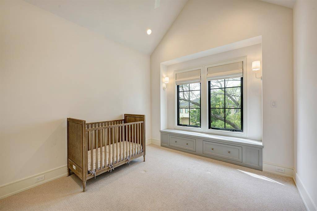 This charming secondary bedroom features a dramatic vaulted ceiling and plush carpeting. Natural light pours in through two large windows that overlook the front lawn and tree-lined street. A custom built-in window seat—complete with hidden storage—adds both charm and functionality, while elegant wall sconces frame the space. Custom window treatments from The Shade Store provide the perfect finishing touch, seamlessly blending comfort with timeless style.
