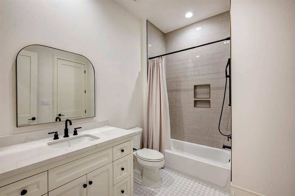 The ensuite bath is equally stylish and functional, featuring a Statuario quartz countertop, designer arched mirror, and matte black fixtures that pop against the soft, neutral tones. The bathtub/shower combination is surrounded by glossy taupe subway tile with a built-in shampoo niche, and a walk-in closet with custom built-in shelving completes the suite.