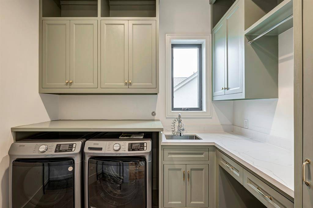 The well-appointed upstairs laundry room features sophisticated custom inset cabinetry finished in designer paint, complemented by premium Statuario quartz countertops. This thoughtfully designed space incorporates a professional-grade stainless steel undermount sink with utility faucet, integrated hamper storage, a convenient built-in drying rack, and dedicated broom storage for optimal organization.