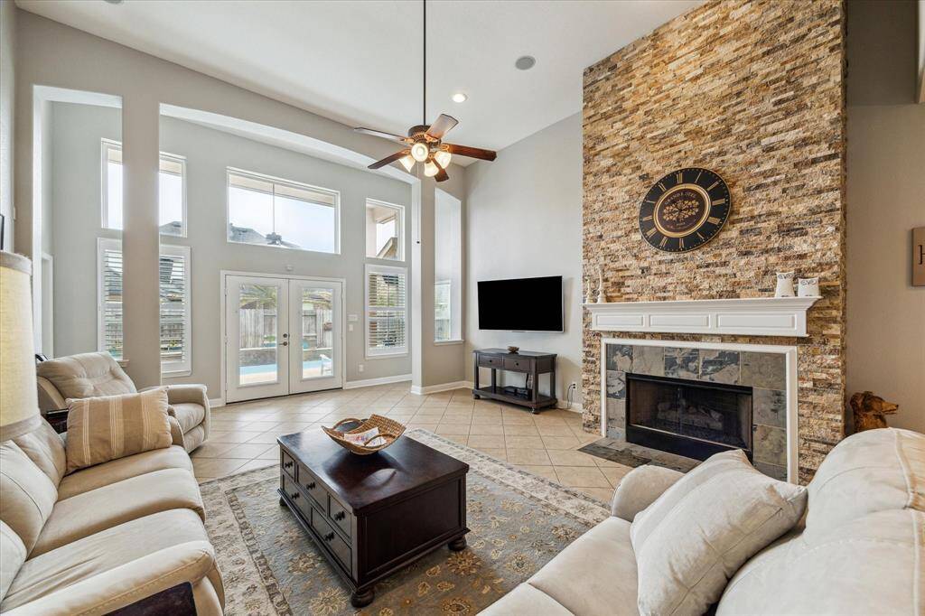 The living room features a stunning stone floor to ceiling fireplace, soaring high ceiling, recessed lighting, and amazing windows including French doors providing a lovely view of your backyard.