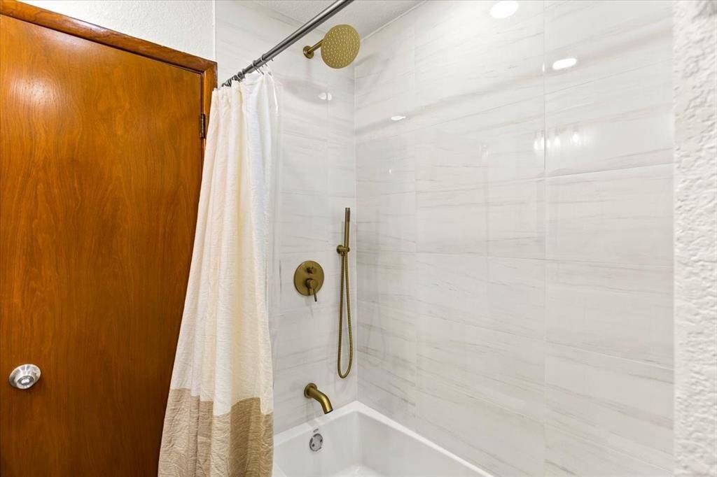 Bathroom with a tub-shower combo, featuring elegant beige tiles and a sleek bronze shower fixture.
