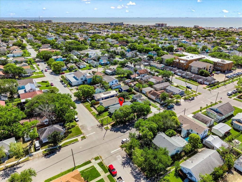 This aerial photo showcases a charming neighborhood with tree-lined streets and a view of the coastline in the distance. The highlighted property is centrally located, nestled among similar well-maintained homes, offering a suburban feel with nearby amenities.