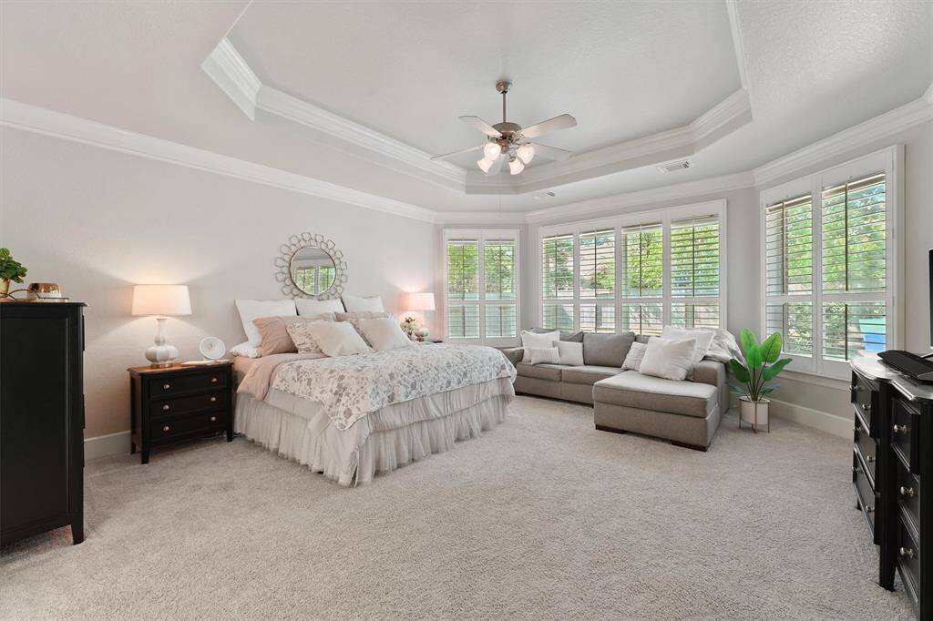 This spacious primary suite features large bay windows, coffered ceilings, and plush carpet to relax and unwind.