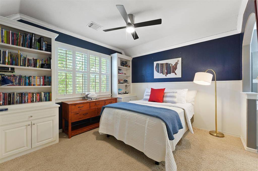 Secondary bedroom with ceiling fan, crown molding, plush carpet, and large window for natural lighting.