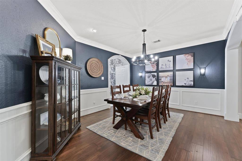 The dining room features wainscot paneling and crown molding. The lighting includes wall scones, an elegant light fixture, and recessed lighting to set the mood.
