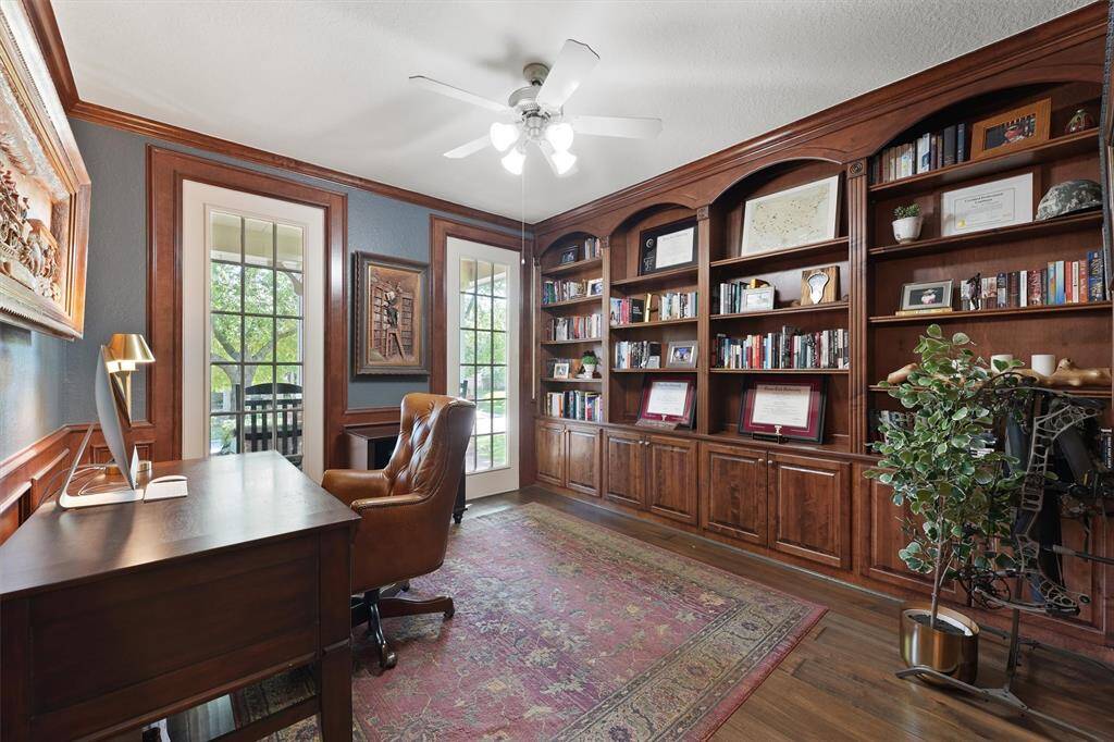 The home office features a custom built-in bookshelf with floor to ceiling windows, and wooden paneling and crown molding throughout the study.