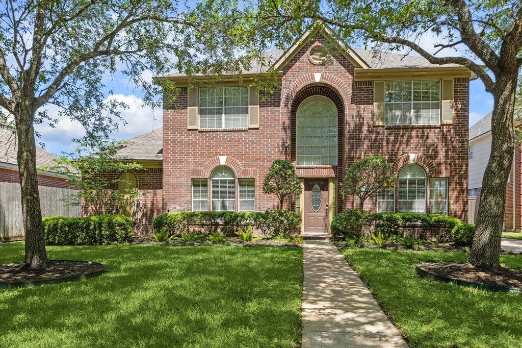 Charming two-story home framed by majestic oak trees and a beautifully manicured lawn.