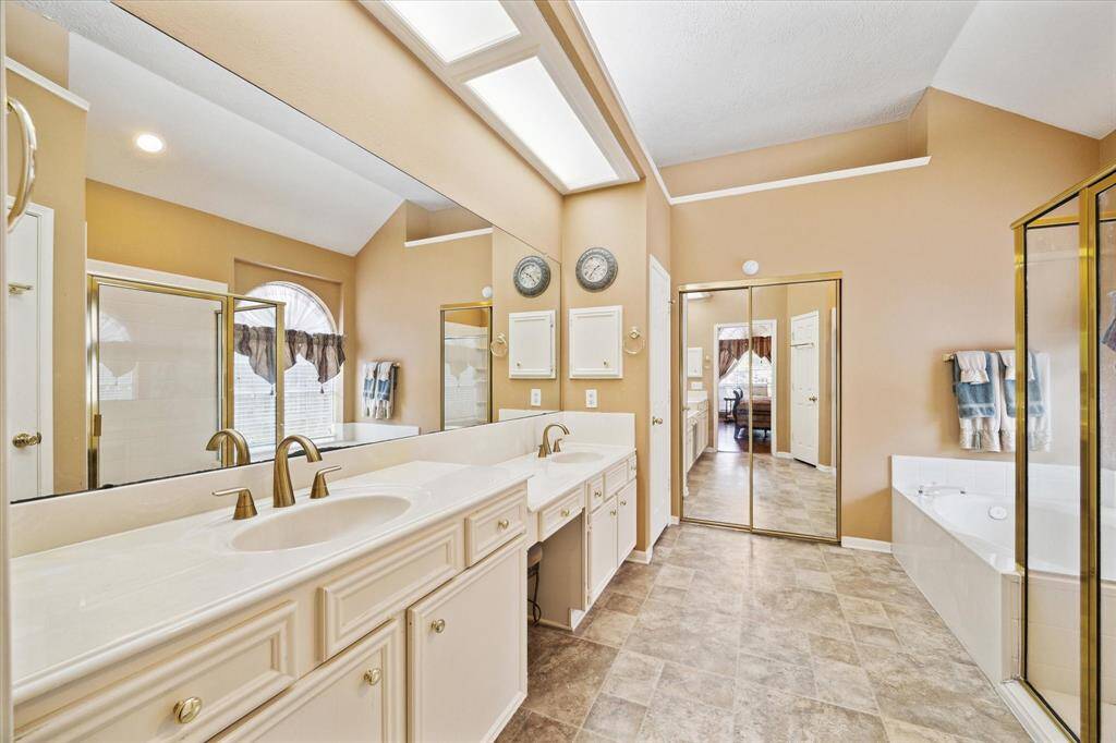 Luxurious bathroom featuring a tiled floor, dual sinks, a jetted tub, separate shower and walk-in closet.