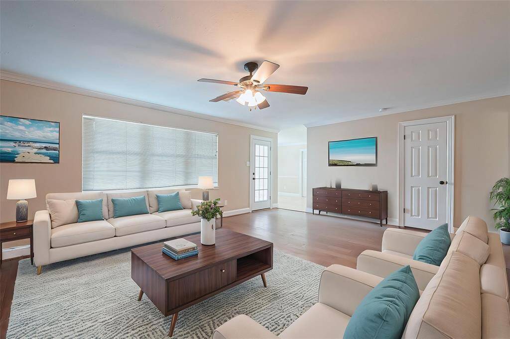 Virtually staged. Bright and spacious living room with neutral walls, engineered wood floors, and a ceiling fan. Features large windows for natural light and easy access to the backyard and the kitchen.