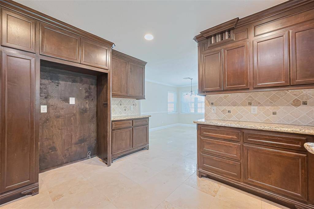 This kitchen features, rich, dark wood cabinetry complemented by a stylish tile backsplash. Ample natural light flows in from adjoining dining area, creating a bright and inviting space.