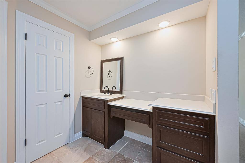 Primary bathroom features a modern double vanity with dark wood cabinets, a single sink, and ample counter space. It includes a framed mirror, recessed lighting, and Travertine flooring, creating a clean and functional space.