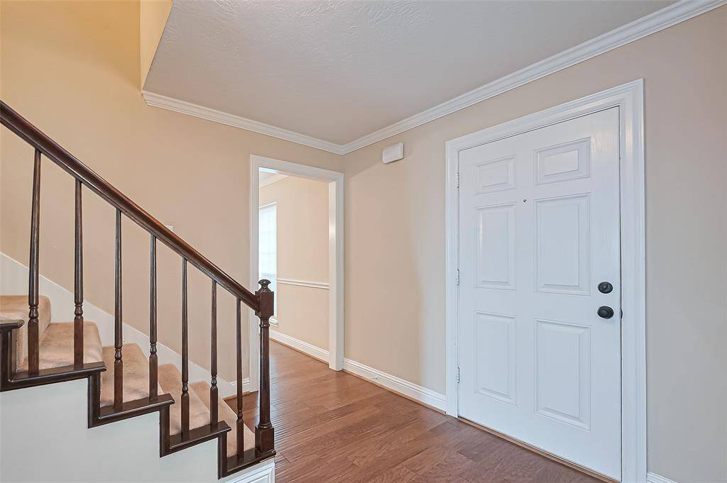 Bright entryway featuring engineered wood floors, neutral walls, and white trim. A staircase with dark wood railing leads upstairs, while the formal dining room is to right and study to the left.