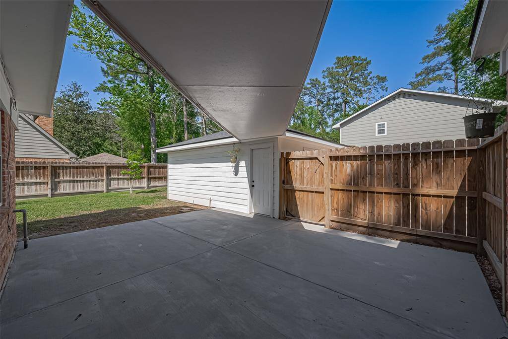 This photo showcases a covered patio area with a concrete floor, leading to a fenced backyard with a lawn and trees.