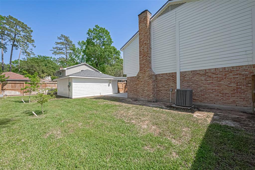 This backyard features a well-maintained lawn, a detached garage, and a brick exterior on the main house. It is bordered by a wooden fence and surrounded by mature trees, providing a sense of privacy and natural beauty.