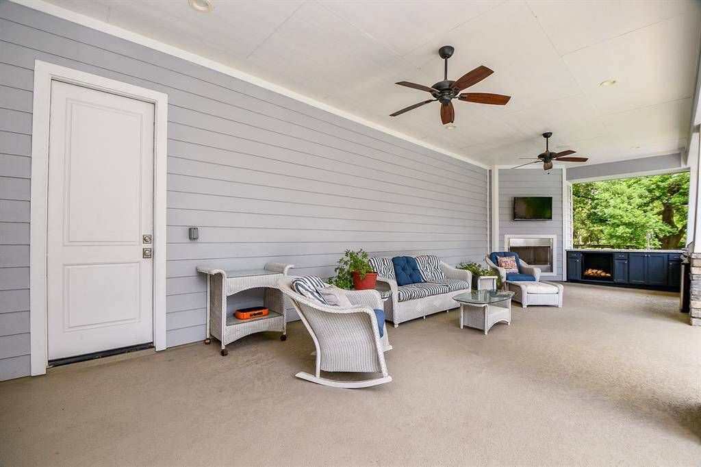 Spectacular covered patio with a cozy seating area, featuring a fireplace, ceiling fans, and a TV. The private setting is perfect for outdoor entertaining. Easy access from the garage.