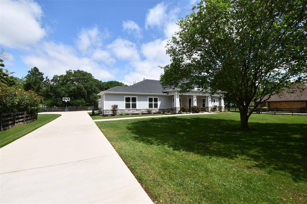 The wide driveway leads to a beautifully maintained one-story home, framed by lush landscaping and mature trees. The expansive front yard creates a peaceful, open feel with just the right touch of privacy.
