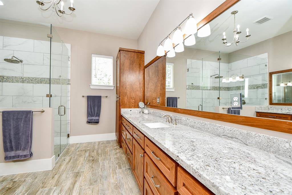 The Primary bathroom features a spacious design with dual sinks, highlighting gorgeous granite countertops, and ample wooden cabinetry for storage. The room is well-lit with modern fixtures.