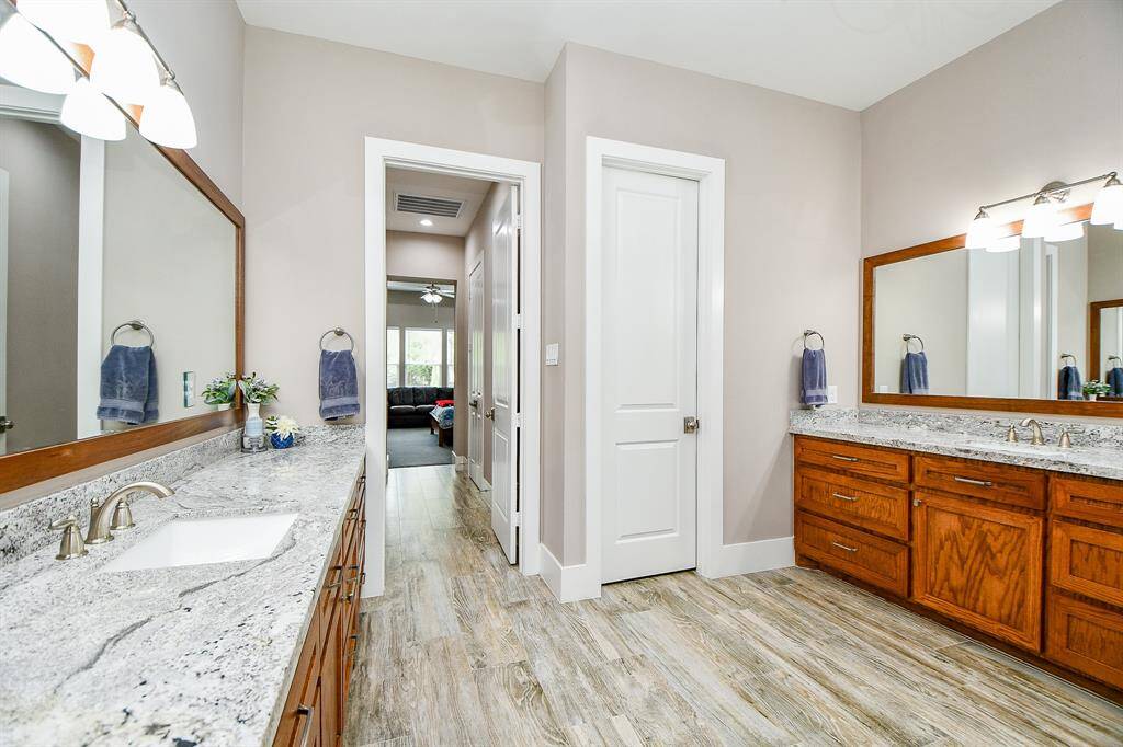 This spacious bathroom offers dual granite-topped vanities, abundant cabinetry, and elegant finishes throughout. Convenient layout flows directly into the adjoining bedroom.