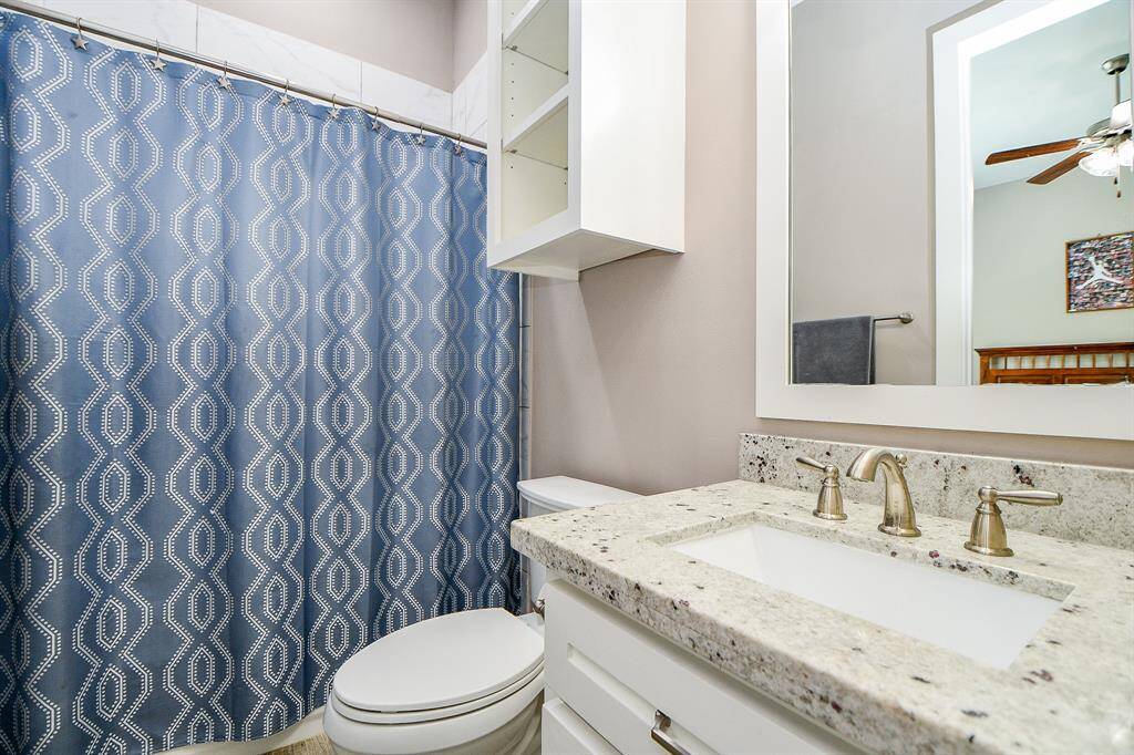 This bathroom features a granite countertop, tub/shower combination, built in shelves, framed mirror with a modern sink and fixtures.