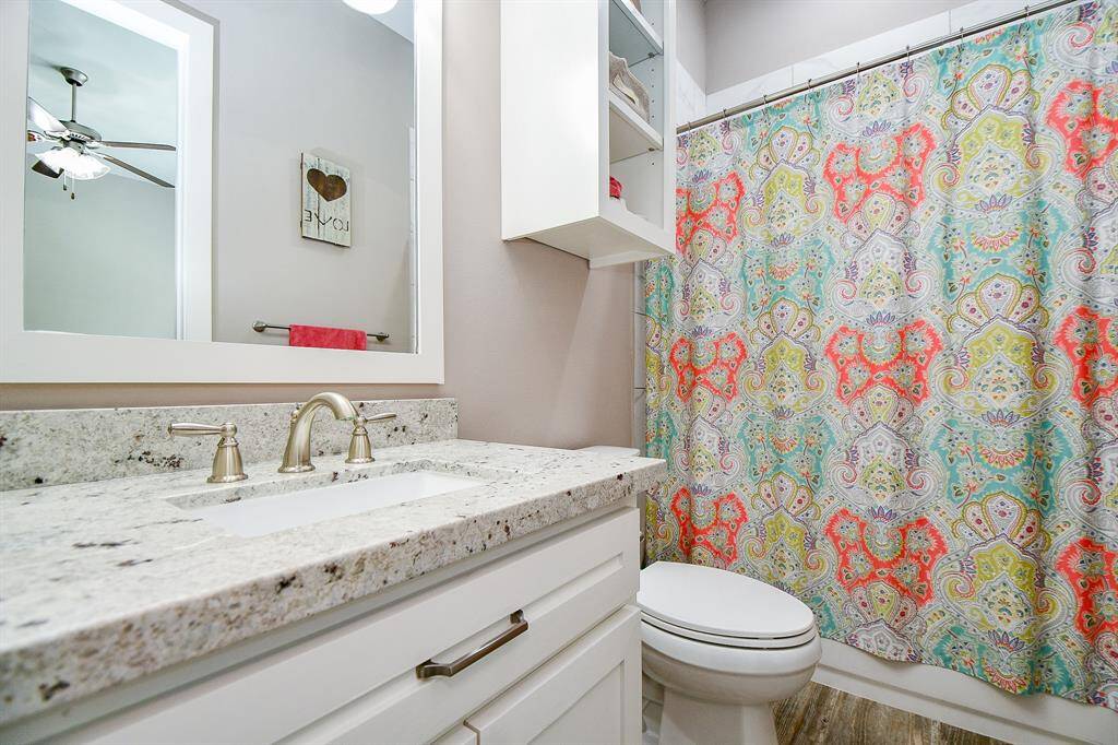 This bathroom features a modern design with granite countertop, tub/shower combination, built in shelves, framed mirror with a modern sink and fixtures.