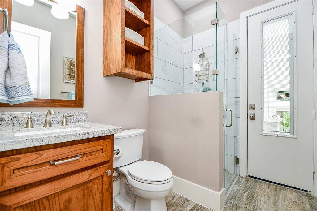 This modern bathroom features a sleek glass-enclosed shower, granite countertop, and warm wood cabinetry. With direct access to the patio, it’s ideal for quick rinses after a swim or convenient outdoor entry.