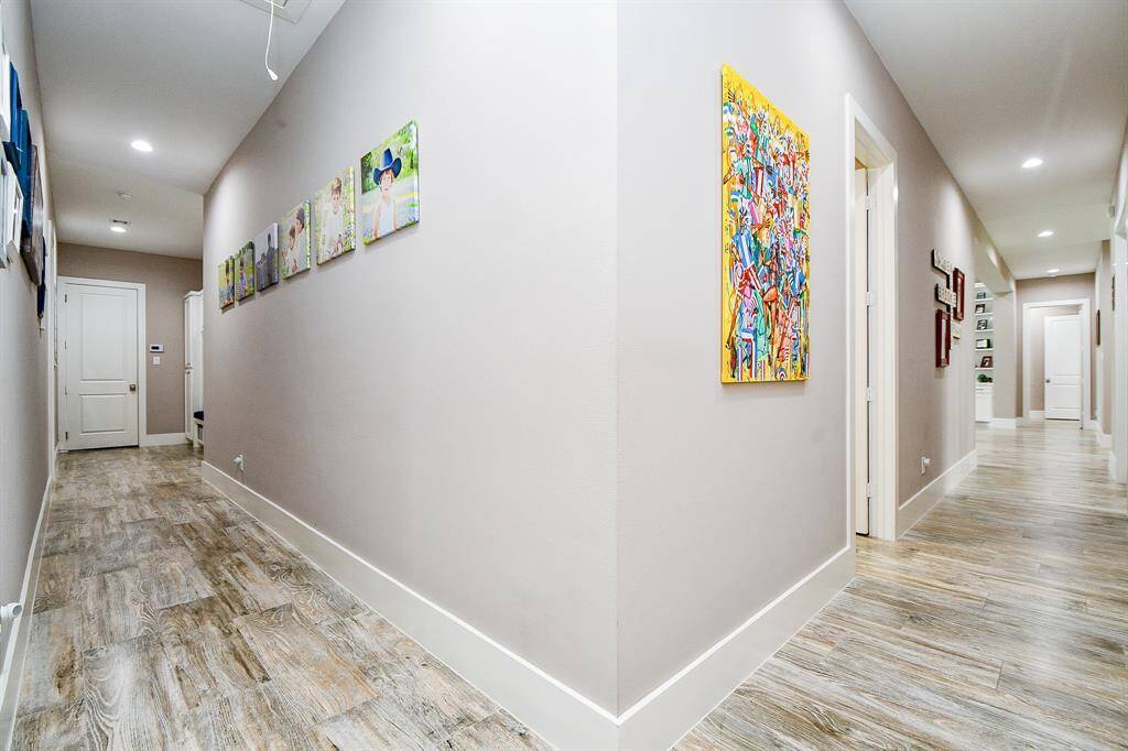 This inviting hallway offers a modern wood-look tile floor, recessed lighting, and ample wall space perfect for art or family photos. Its open, airy feel adds flow and warmth to the home’s layout.
