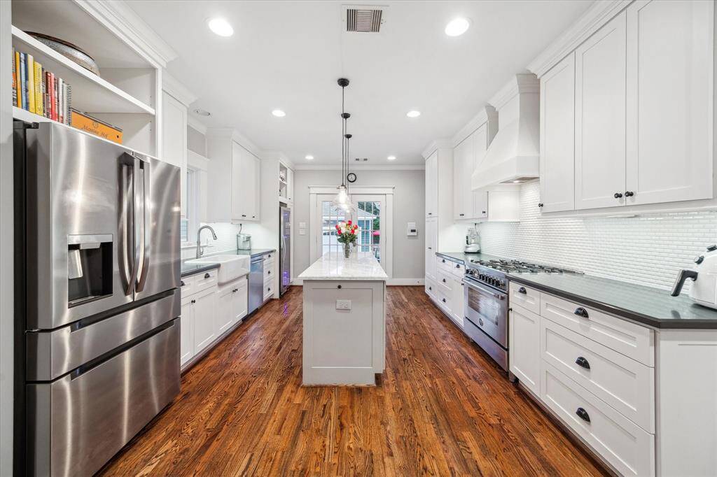 This well-appointed kitchen features an island with a marble countertop and contrasting black caesar stone countertops for the rest of the kitchen.  There is an abundance of cabinet and drawer space, stylish backsplash, and under-cabinet lighting.