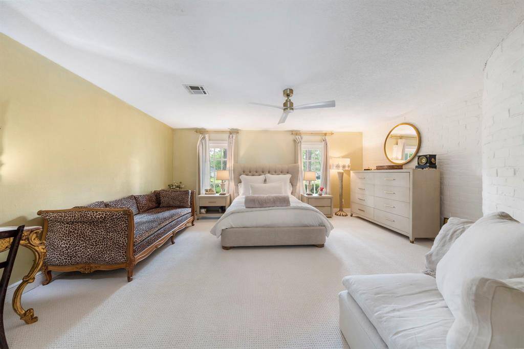 First-floor primary suite, thoughtfully tucked away for privacy, featuring charming white-painted brick accents, fresh Berber carpet, and a spacious walk-in closet.