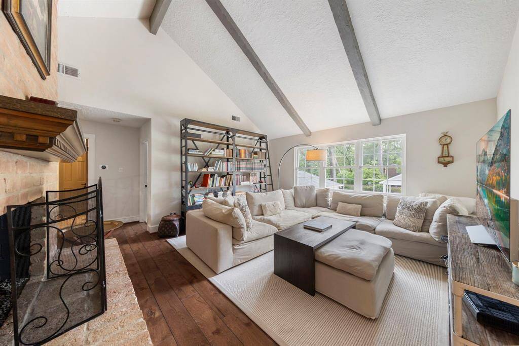 Upstairs, a spacious game room awaits, featuring a vaulted ceiling, a cozy brick gas log fireplace, rich wood floors, and large windows offering stunning views of the backyard.