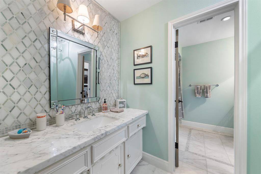 Updated vanity space with a sleek tile backsplash extending to the ceiling, complemented by modern fixtures for a stylish, polished look.