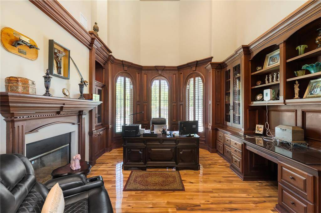 This stunning home office strikes the perfect balance between functionality and elegance. Soaring arched windows flood the space with natural light, creating an inviting atmosphere for work or study. Rich wood-paneled built-ins add warmth and character, while the stately fireplace serves as a striking focal point, enhancing the room’s refined sophistication.