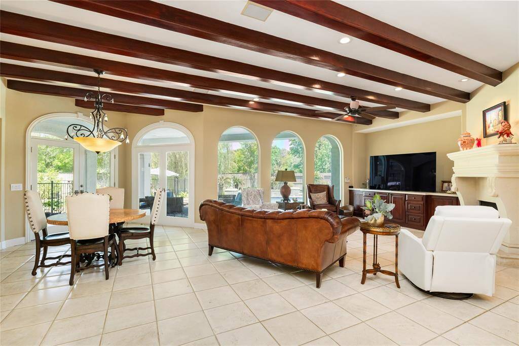 This spacious living area features elegant tile flooring, exposed wood beams, and large arched windows offering plenty of natural light. The open layout includes a dining space, perfect for entertaining.