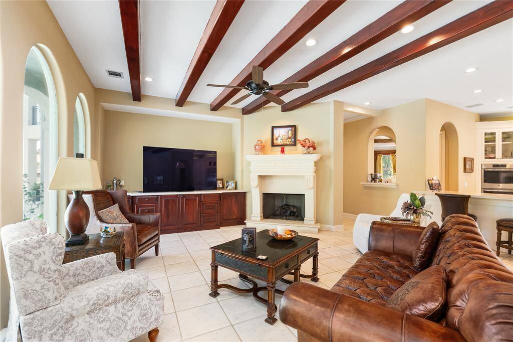 This spacious living room features elegant wood beam ceilings, a cozy fireplace, and large arched windows.