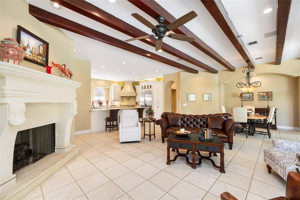 This spacious living area features a cozy fireplace, exposed wooden beams, and tile flooring. It seamlessly connects to a modern kitchen with a breakfast bar and an adjacent dining space, creating an open-concept feel perfect for entertaining.