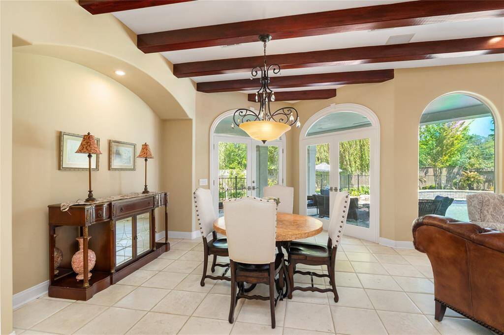 This inviting breakfast area seamlessly blends style and comfort, offering the perfect spot to enjoy morning coffee or casual meals. Framed by graceful arched windows and French doors, the space is drenched in natural light and showcases stunning views of the backyard oasis. Rich wood ceiling beams add architectural charm, while the elegant chandelier and classic furnishings complete the room’s warm, timeless appeal.