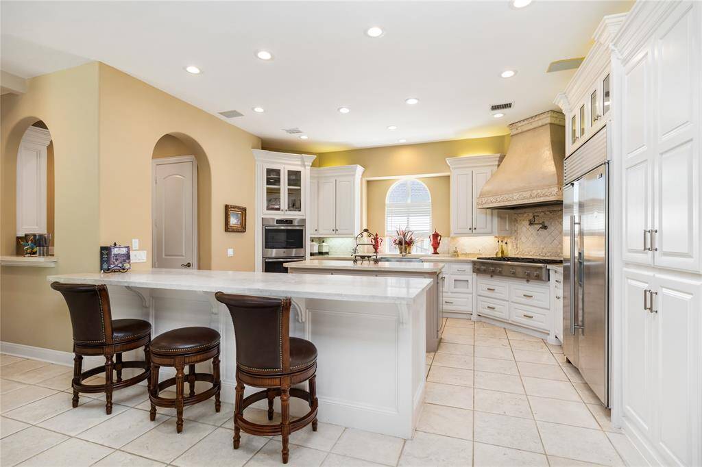 This expansive kitchen is both stylish and functional, featuring a generous granite island, top-of-the-line stainless steel appliances, and an abundance of custom cabinetry for effortless organization. Bathed in natural light and accented by recessed lighting, the space feels bright and welcoming. Elegant touches like the custom range hood and graceful arched doorways elevate the kitchen’s timeless, sophisticated design.