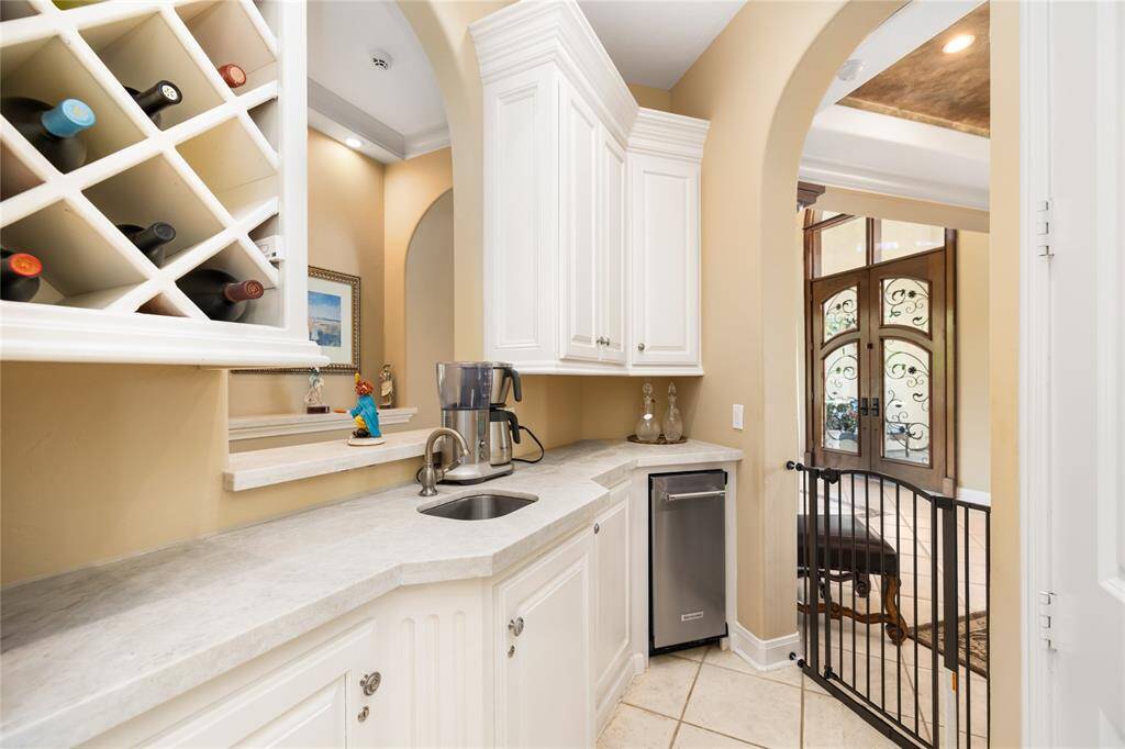 The wet bar, conveniently located off the kitchen and dining area, is equipped with a sleek countertop, wine rack, sink, and beverage cooler. The arched doorway offers a preview of the bright and welcoming entrance beyond.