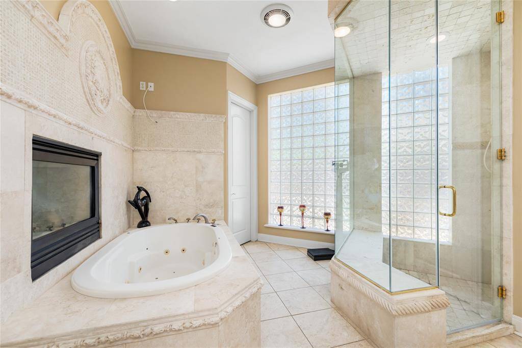 Indulge in the ultimate relaxation within this luxurious primary bathroom, where the spacious, jetted soaking tub invites you to unwind in style. Positioned next to a cozy fireplace, it offers the perfect ambiance for a peaceful retreat. A large window floods the room with beautiful natural light, enhancing the elegant, serene atmosphere—imagine unwinding in this sophisticated space at the end of a long day.