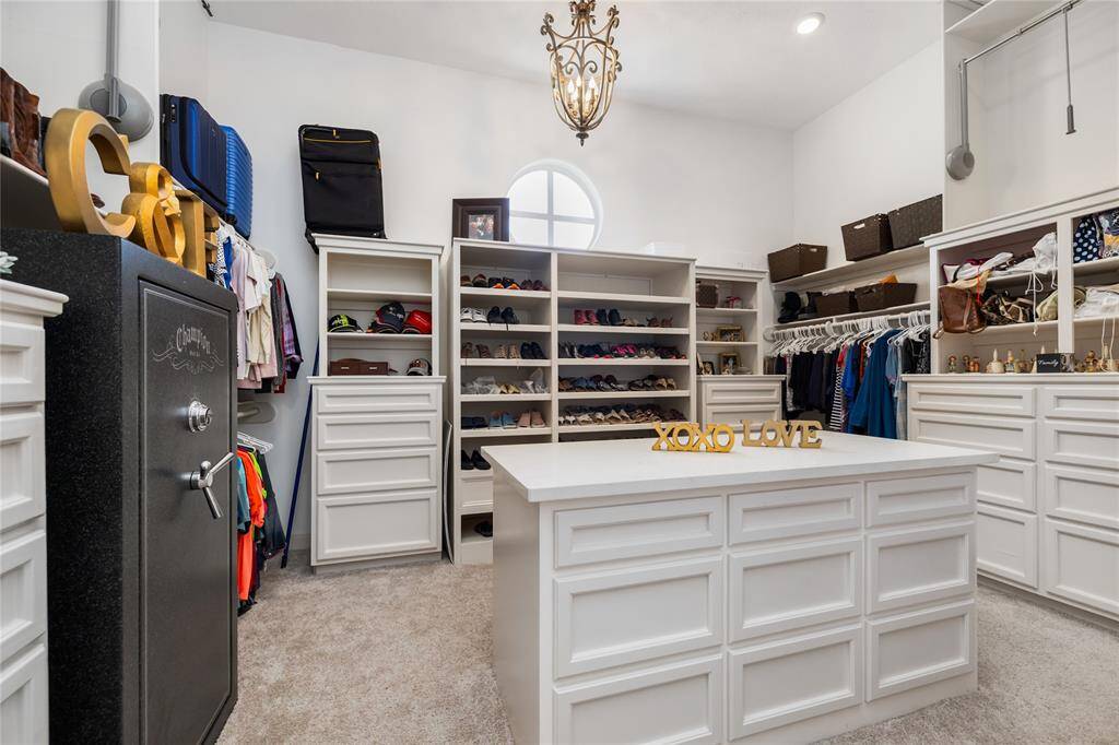 Step into this breathtaking primary closet, where expansive built-ins offer ample storage with custom shelving and drawers, providing both organization and elegance. The plush carpeting adds a soft touch, while the sophisticated light fixture illuminates every corner of this all-white space. A center island of drawers adds extra storage and convenience, completing this beautifully designed, well-lit sanctuary.