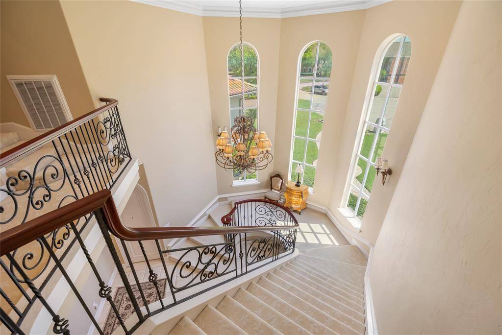 This grand staircase, featuring elegant iron railings and plush carpeting, sets the tone for the home's sophisticated design. Tall arched windows flood the space with natural light, beautifully illuminating the stunning chandelier and inviting seating area below, creating an elegant and welcoming entryway.