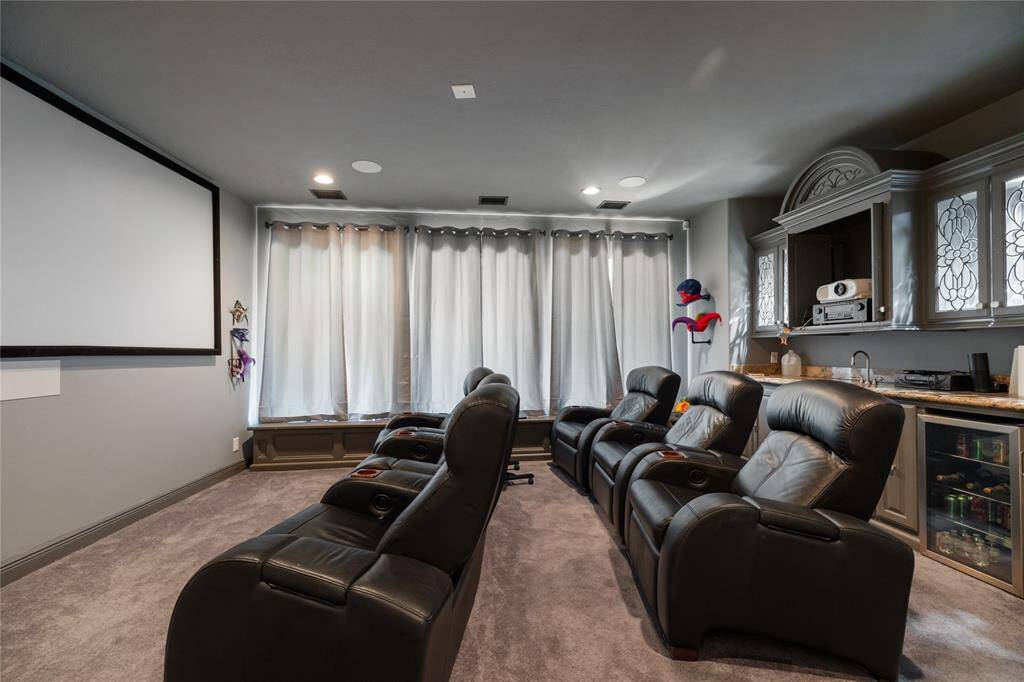 This home theater room offers the perfect setting for relaxation and entertainment, featuring a large screen and sleek design. A bar area with a mini-fridge and sink adds convenience, while elegant cabinetry and soft lighting create an inviting, sophisticated atmosphere.