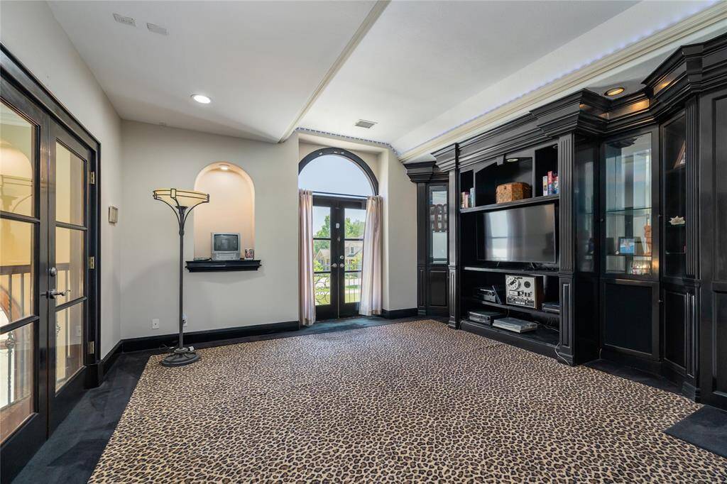 This expansive game room exudes luxury and style, featuring dark wood cabinetry with a built-in entertainment center. A large arched window fills the space with natural light, highlighting the room creating an inviting, sophisticated atmosphere.