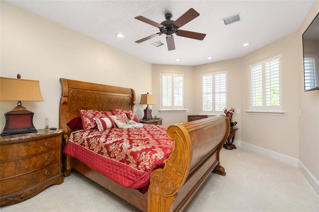 This cozy bedroom features large windows with plantation shutters offer plenty of natural light, while a ceiling fan adds comfort and style.