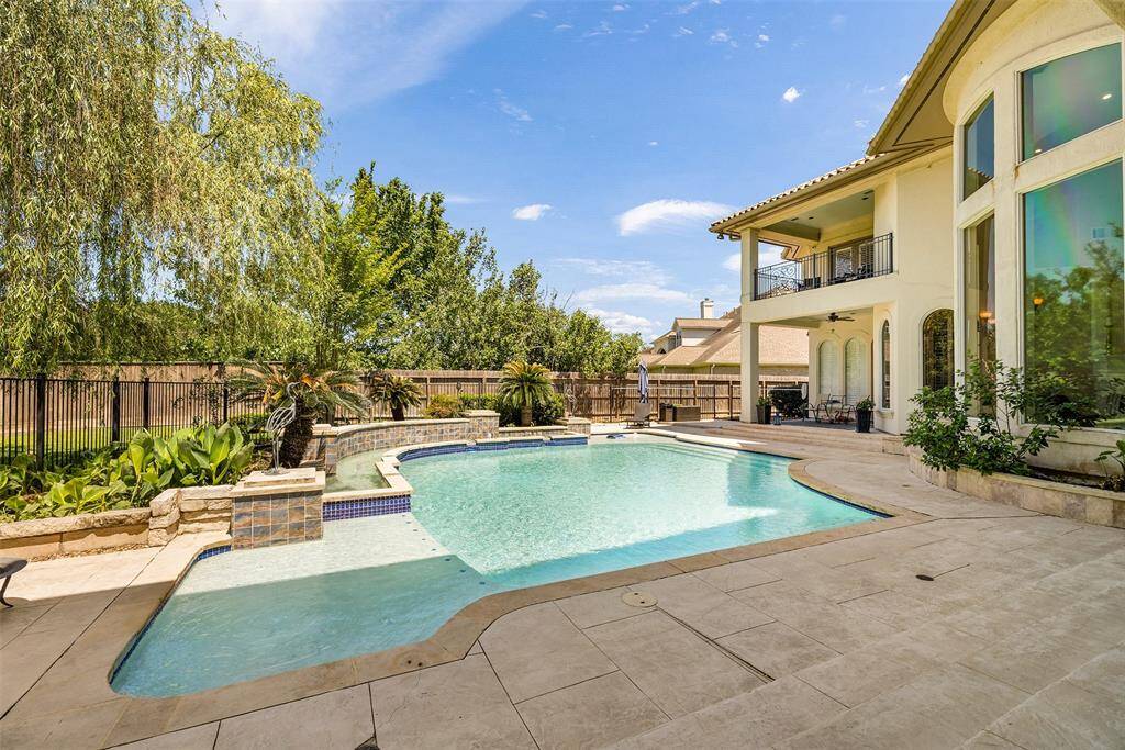 The pool is surrounded by lush landscaping and an elegant stone patio.