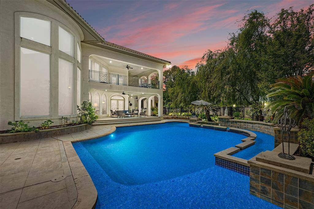 This stunning home features a spacious outdoor area with a beautifully designed pool, surrounded by lush greenery. With large windows, elegant balconies, and a covered patio, the backyard is perfectly poised for entertaining or relaxing.