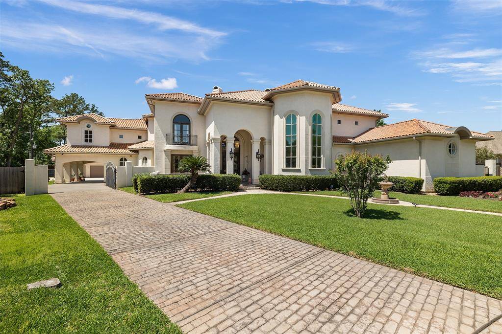 This impressive Mediterranean-style home features a grand entrance, arched windows, and a beautiful tile roof. It includes a spacious driveway, well-maintained landscaping, and a lush green lawn, offering curb appeal and elegance.